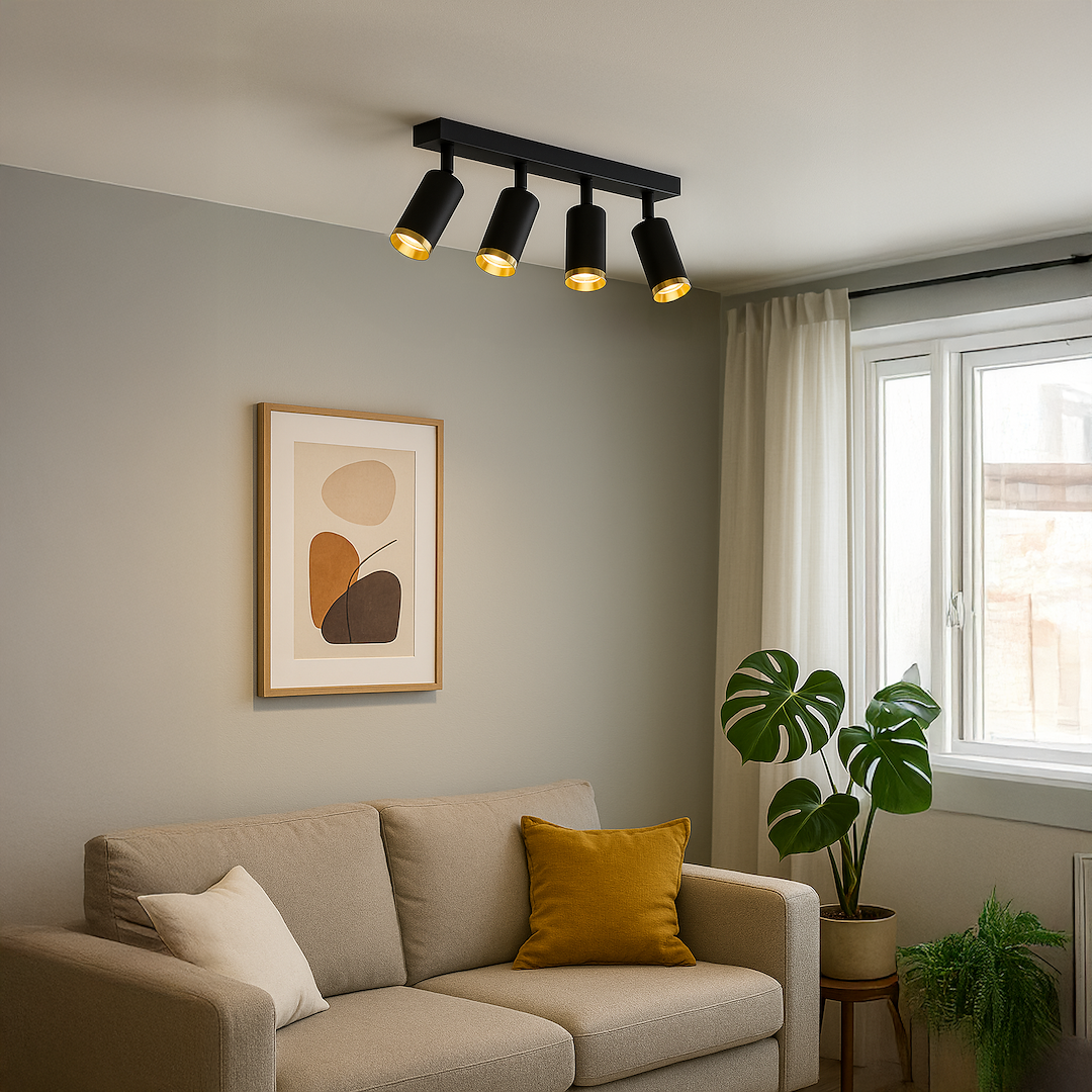 Lampa sufitowa Mica w kolorze czarnym z złotymi akcentami, składająca się z czterech reflektorów GU10, zamontowana na prostokątnej podstawie. Widok z boku, w aranżacji z jasną sofą i roślinami w tle.