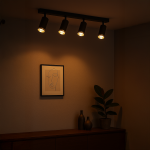 Czarna lampa sufitowa (spot) Mica z czterema oprawami na żarówki GU10, zamontowana na prostokątnej podstawie. W tle widoczna dekoracja w postaci grafiki i roślina w doniczce, na drewnianym meblu. Oświetlenie emitujące ciepłe światło.