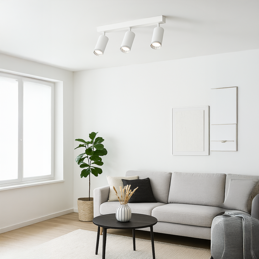 Lampa sufitowa Mica w kolorze białym i chromowanym, z trzema reflektorami GU10. Zamontowana na prostokątnej podstawie, w aranżacji nowoczesnego wnętrza z szarym sofą i rośliną doniczkową.