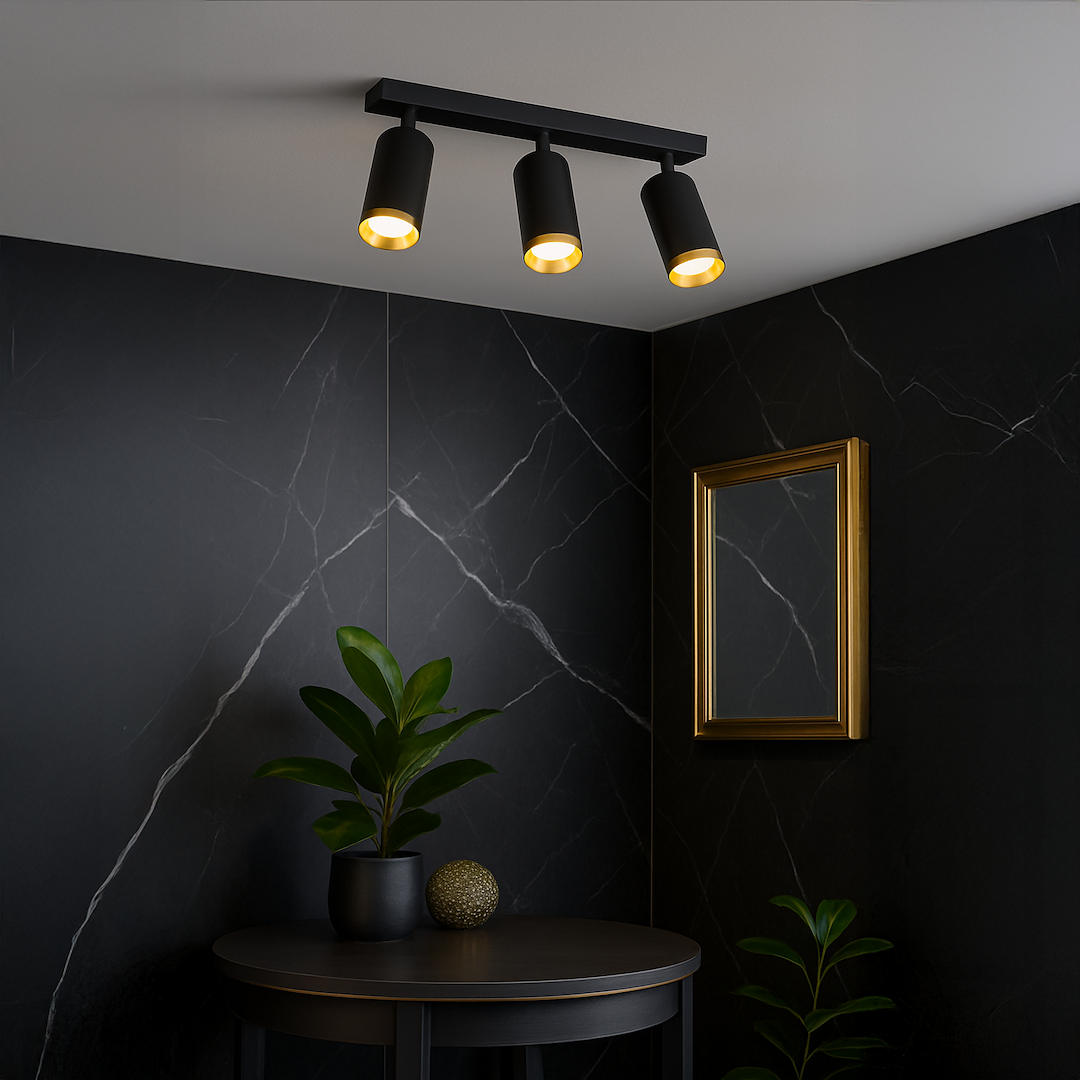 Lampa sufitowa Mica z trzema reflektorami GU10 w kolorze czarnym z złotymi detalami. Zamontowana na suficie, z jasnym światłem skierowanym w dół. W tle widoczna ciemna ściana z marmurowym wzorem oraz rośliny w doniczkach na stoliku.