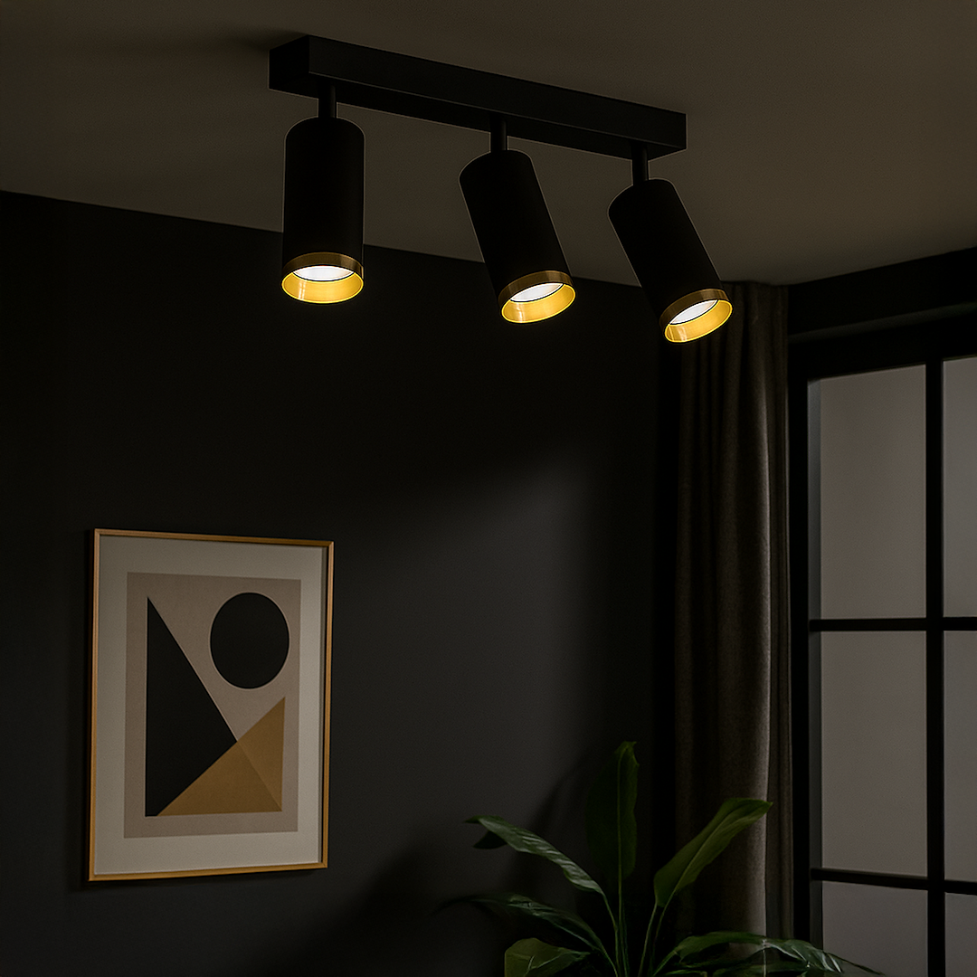 Czarna lampa sufitowa Mica z trzema reflektorami GU10, w złotych wnętrzach kloszy. Ujęcie z przodu, zamontowana na ścianie, w otoczeniu grafiki i rośliny. Tło w ciemnych odcieniach z zasłonami.