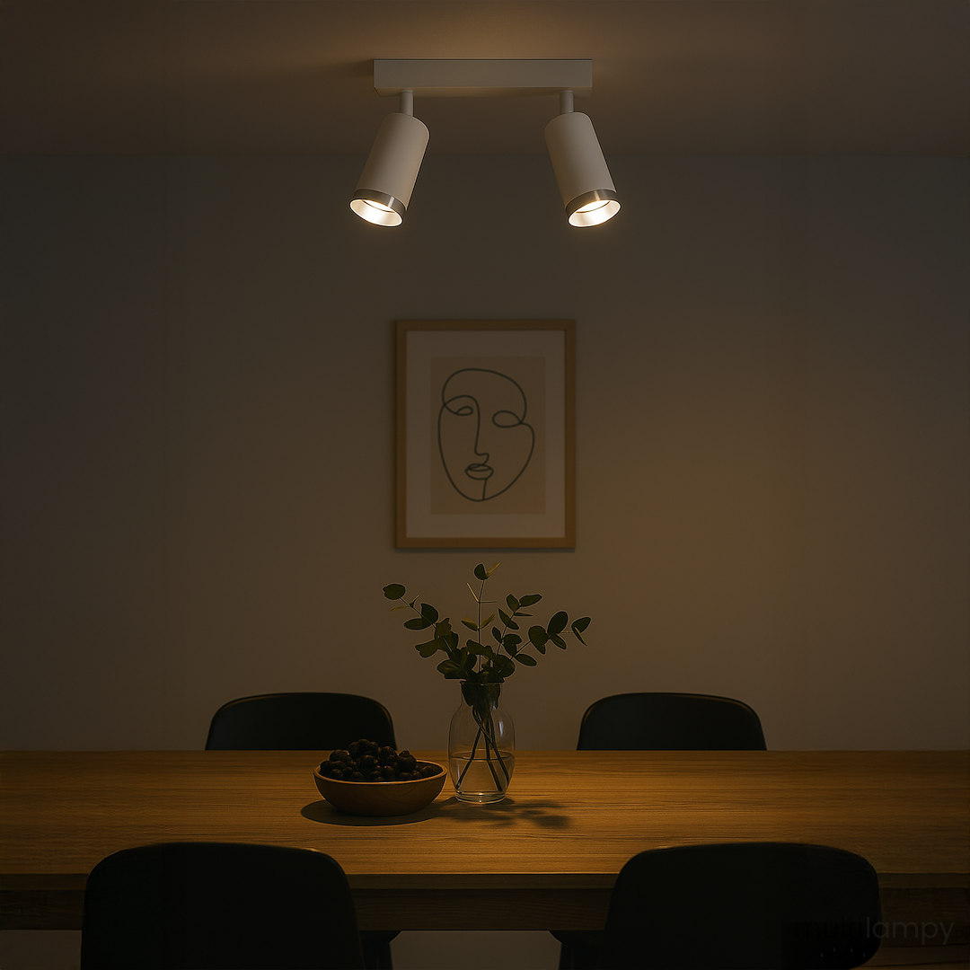 Lampa sufitowa Mica w kolorze białym i chromowanym, z dwoma punktami świetlnymi GU10, zamontowana na prostokątnej podstawie. Ujęcie z góry, oświetlająca stół z drewnianym blatem, w otoczeniu czarnych krzeseł i dekoracji.