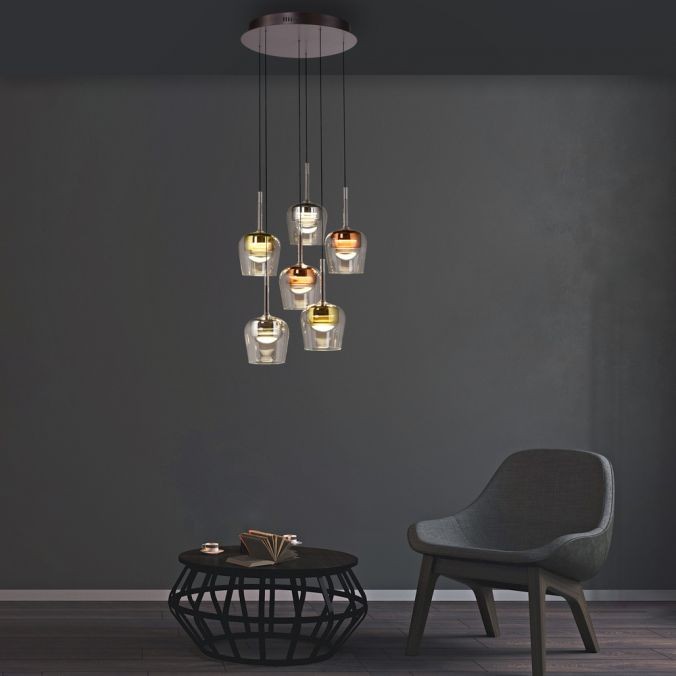 Lampa wisząca Q-kon z pilotem, 6 kloszy LED w różnych kolorach, zawieszona na cienkich linkach. Okrągła podsufitka o ciemnym wykończeniu. W tle szara ściana oraz nowoczesne, ciemne meble.