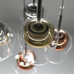 Lampa wisząca Q-kon z pilotem, z sześcioma źródłami LED w różnych kolorach. Szklane klosze w kolorze przezroczystym i mosiężnym, zawieszone na metalowych linkach. Kąt ujęcia z góry, podkreślający detale konstrukcji i wykończenia.
