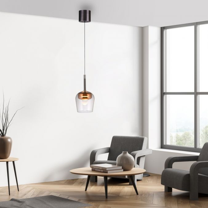 Lampa wisząca Q-kon z pilotem LED 9W CCT w kolorze miedzi. Szklany klosz o okrągłym kształcie w przezroczystym i miedzianym wykończeniu, zawieszona na cienkim przewodzie. Wnętrze nowoczesnej aranżacji z sofą i stolikiem.
