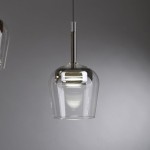 Lampa wisząca Q-kon z pilotem LED 9W CCT w srebrnym kolorze, o szklanej, przezroczystej obudowie w kształcie dzwonu. Zawieszona na cienkim przewodzie, przedstawiona z boku, w minimalistycznym otoczeniu.