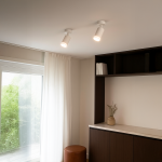 Biała lampa sufitowa Pipe Ring z jedną oprawą GU10, zamontowana pod kątem na suficie. W tle widoczna półka z książkami oraz jasne zasłony przy oknie. Lampa o prostym, cylindrycznym kształcie, zapewniająca skupione światło.