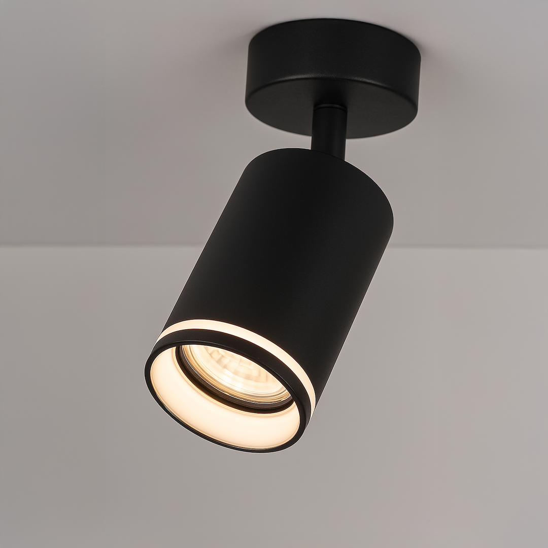 Lampa sufitowa Pipe Ring w czarnym kolorze, z cylindrycznym kloszem, montowana na suficie. Wewnątrz widoczna żarówka GU10, emitująca ciepłe światło. Kąt ujęcia z góry, podkreślający minimalistyczny design i nowoczesny styl.