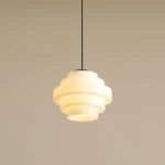 Lampa wisząca Filo w stylu retro, czarna, z oprawą z białego szkła w formie zestawionych pierścieni. Wymiary: średnica 14 cm, wysokość 41 cm. Zawieszona na czarnym przewodzie, na jasnym tle.