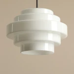 Lampa wisząca Filo w stylu retro, wykonana z białego, błyszczącego materiału. Okrągły, warstwowy kształt, z jednym gniazdem E27. Zawieszona na cienkim czarnym kablu. Wysokość 45 cm, średnica 22 cm. Idealna do nowoczesnych wnętrz.