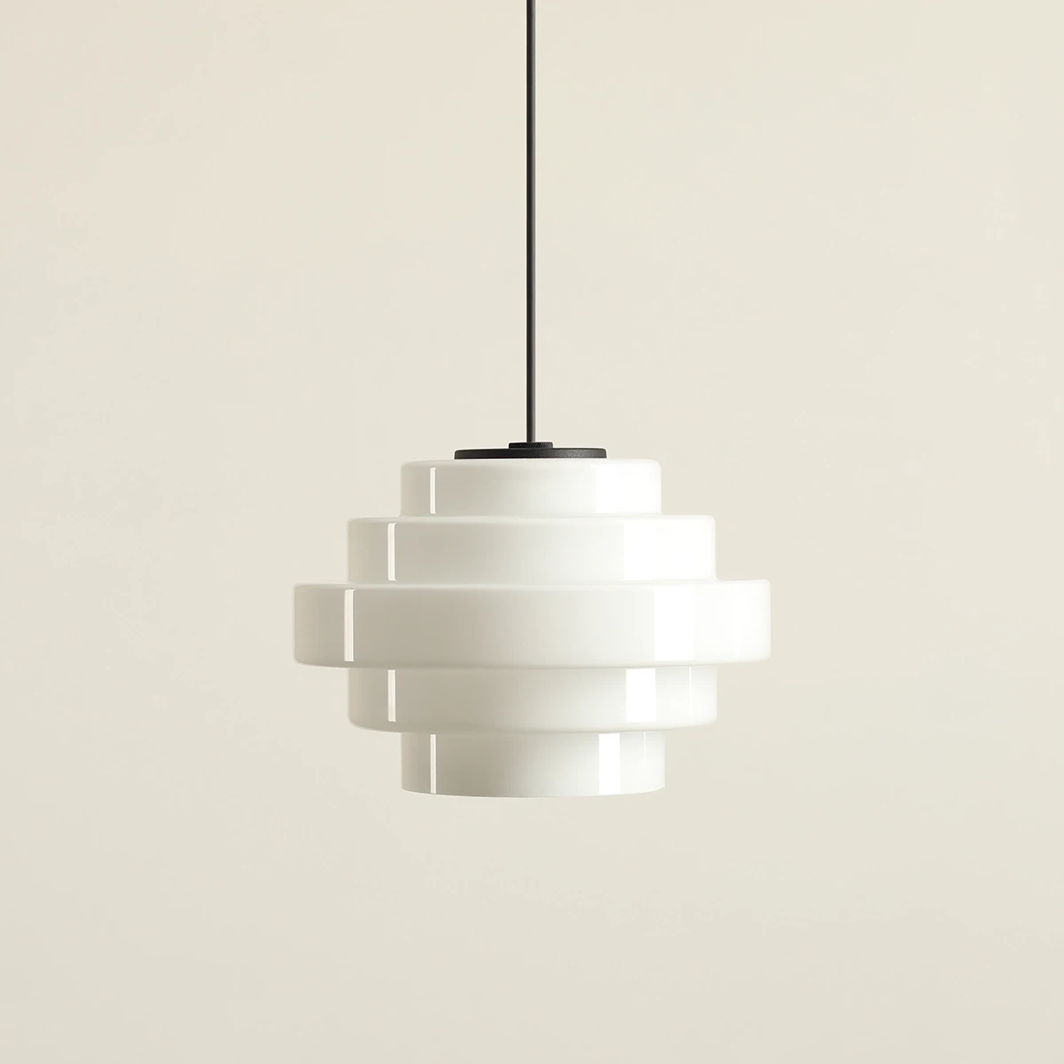 Lampa wisząca Filo w stylu retro, z białego szkła, o cylindrycznym kształcie z warstwowym wzorem. Posiada czarny metalowy uchwyt. Wymiary: średnica 22 cm, wysokość 75 cm. Zawieszona na czarnym przewodzie na jasnym tle.