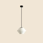 Lampa wisząca Filo w stylu retro z białego tworzywa, o średnicy 22 cm i wysokości 75 cm, zawieszona na czarnym, cienkim kablu. Kształt przypominający warstwy, umieszczona na jednolitym tle.