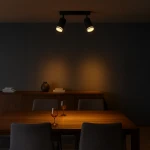 Lampa sufitowa Pipe Ring w kolorze czarnym, z dwoma reflektorami GU10, zamontowana na suficie. Reflektory skierowane w dół, o okrągłym kształcie. W tle drewniany stół z szarymi krzesłami, szklanki i dekoracyjny wazon.