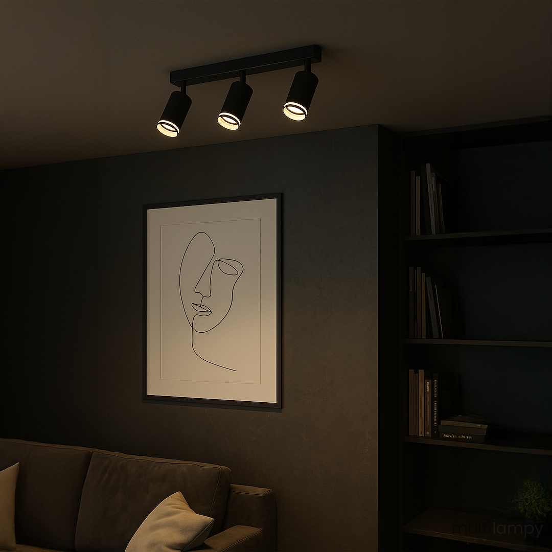 Lampa sufitowa Pipe Ring w kolorze czarnym, z trzema spotami na żarówki GU10, zamontowana na ścianie. W tle widoczny obraz z minimalistycznym rysunkiem i ciemne półki z książkami. Produkt o nowoczesnym designie, idealny do oświetlenia wnętrz.