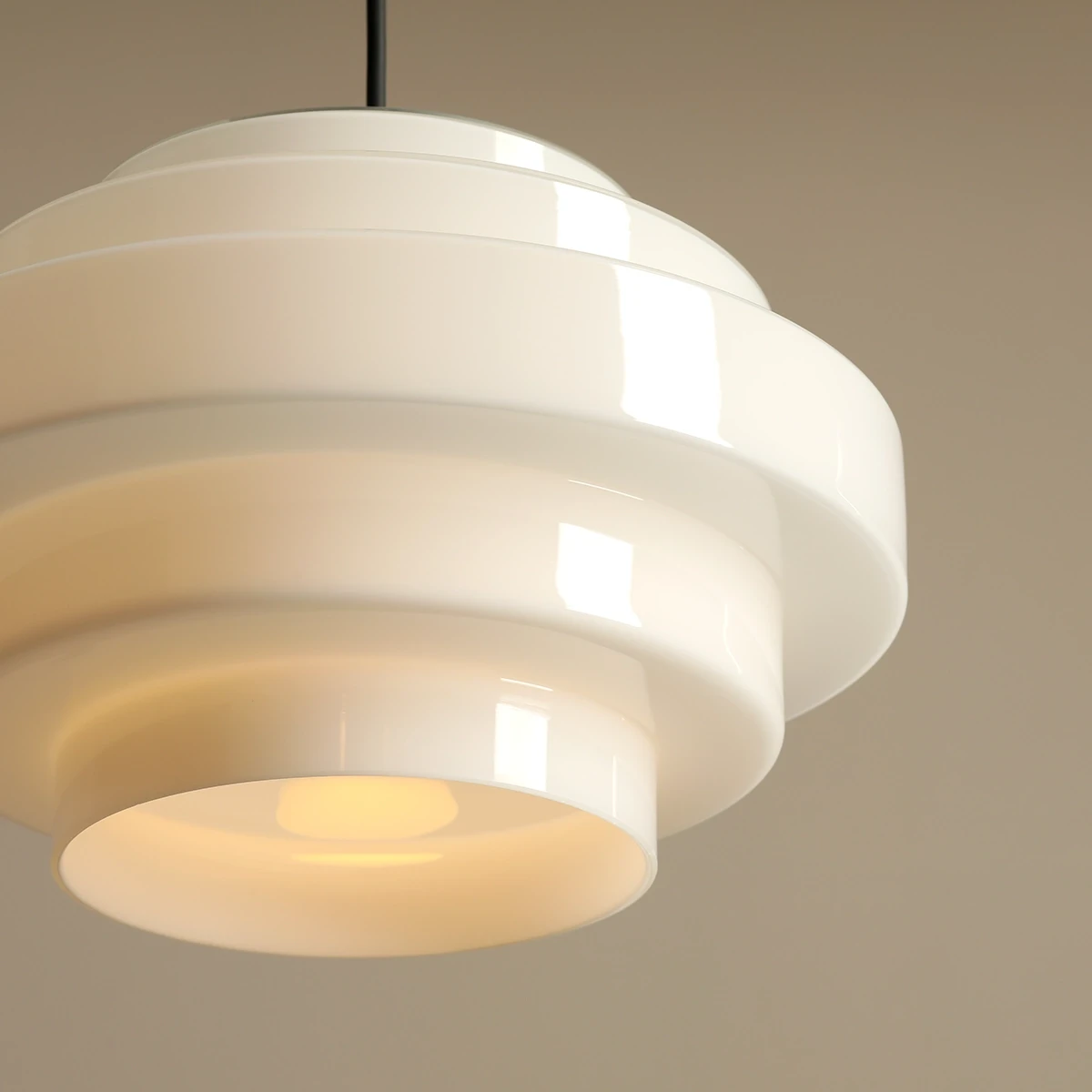 Lampa wisząca Filo w stylu retro, czarna, z metalowym zawieszeniem, w kształcie okrągłej, warstwowej osłony. Wymiary: średnica 28 cm, wysokość 108 cm. Zawiera miejsce na żarówkę E27. Tło jednolite, zbliżenie na detal lampy.