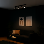 Czarna lampa sufitowa Pipe Ring z czterema reflektorami GU10, montowana na ścianie, o minimalistycznym designie. Ujęcie z boku, w tle widoczne dwa plakaty na ciemnej ścianie oraz sofę z poduszką i stół kawowy z książką.