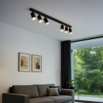 Czarna lampa sufitowa Pipe Ring z sześcioma reflektorami GU10, zamontowana na prostokątnej listwie. Ujęcie z boku, w nowoczesnym wnętrzu z szarym sofą i oknem z widokiem na zieleń. Dwa obrazy na ścianie w minimalistycznym stylu.