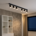 Lampa sufitowa Pipe Ring w kolorze czarnym z sześcioma reflektorami GU10. Zainstalowana na prostokątnej listwie, z widocznym, matowym wykończeniem. Ujęcie z boku w nowoczesnym wnętrzu z szafką i oknem.