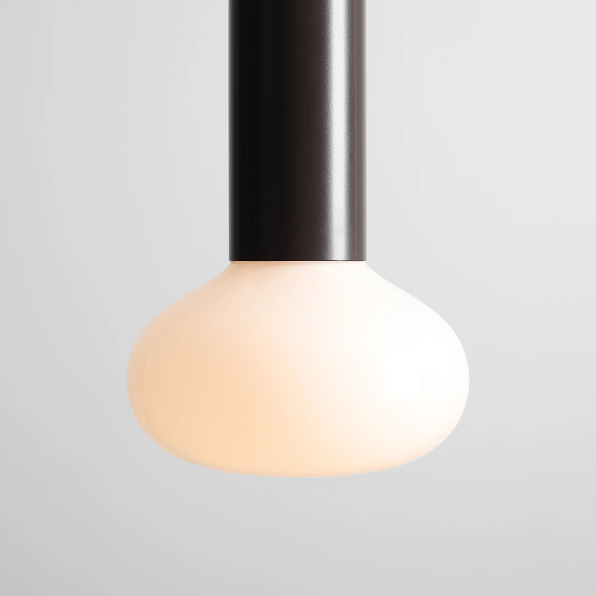 Lampa wisząca Flo Mokka D19 z oprawą w kolorze czarnym i kloszem w kształcie kuli z mlecznego szkła. Produkt zawiera miejsce na żarówkę E14. Ujęcie z bliska, ukazujące detal klosza i mocowania.