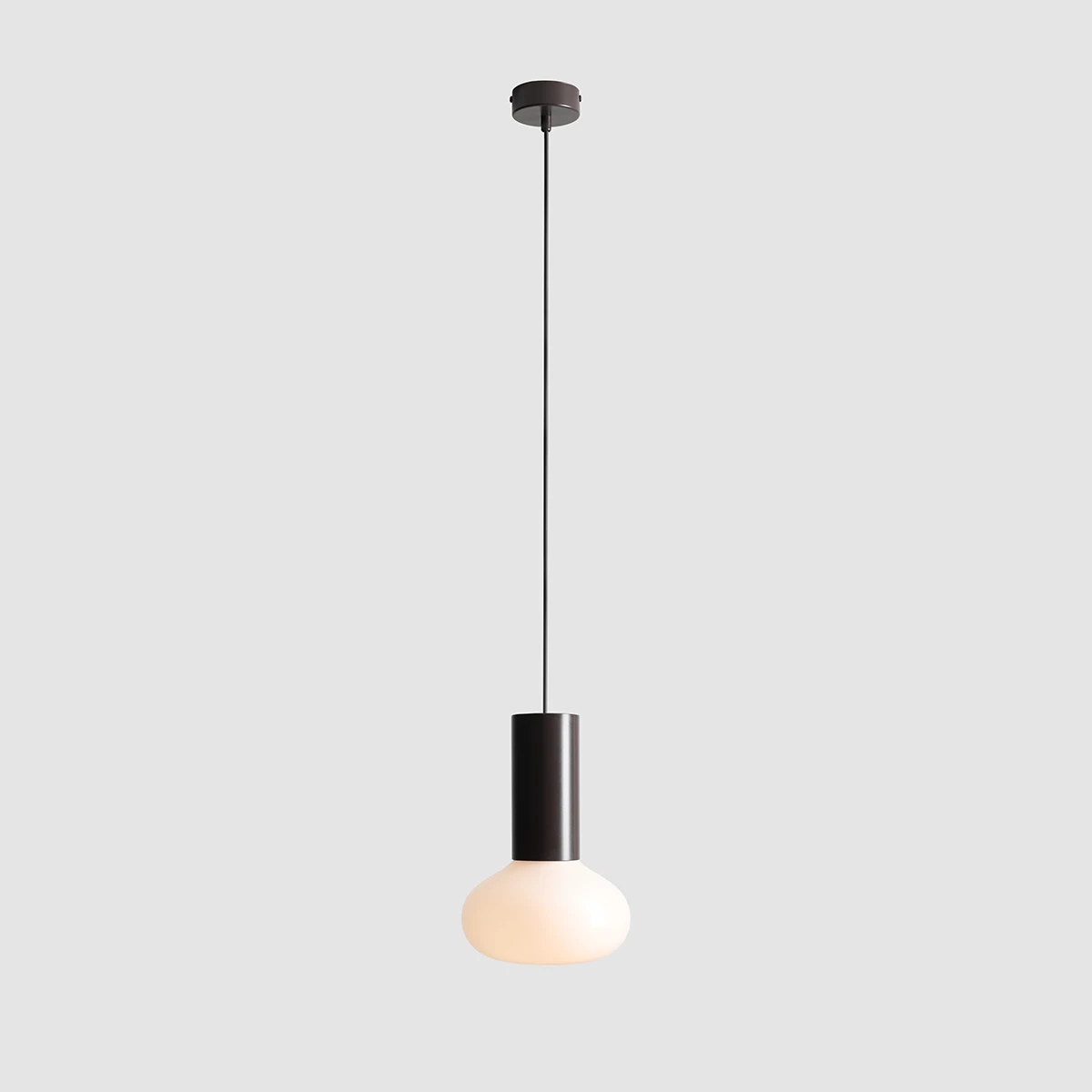 Lampa wisząca Flo Mokka D19 z pojedynczym źródłem światła E14. Posiada czarną metalową podstawę i okrągły, matowy klosz w kolorze białym. Zawieszona na cienkim przewodzie, w prostym, nowoczesnym stylu. Tło jasnoszare.