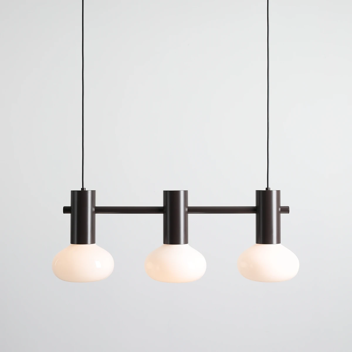 Lampa wisząca Flo Mokka z trzema oprawkami E14, w kolorze ciemnego brązu. Posiada okrągłe, mleczne klosze, zawieszona na cienkim przewodzie. Prosty, nowoczesny design idealny do różnych wnętrz.