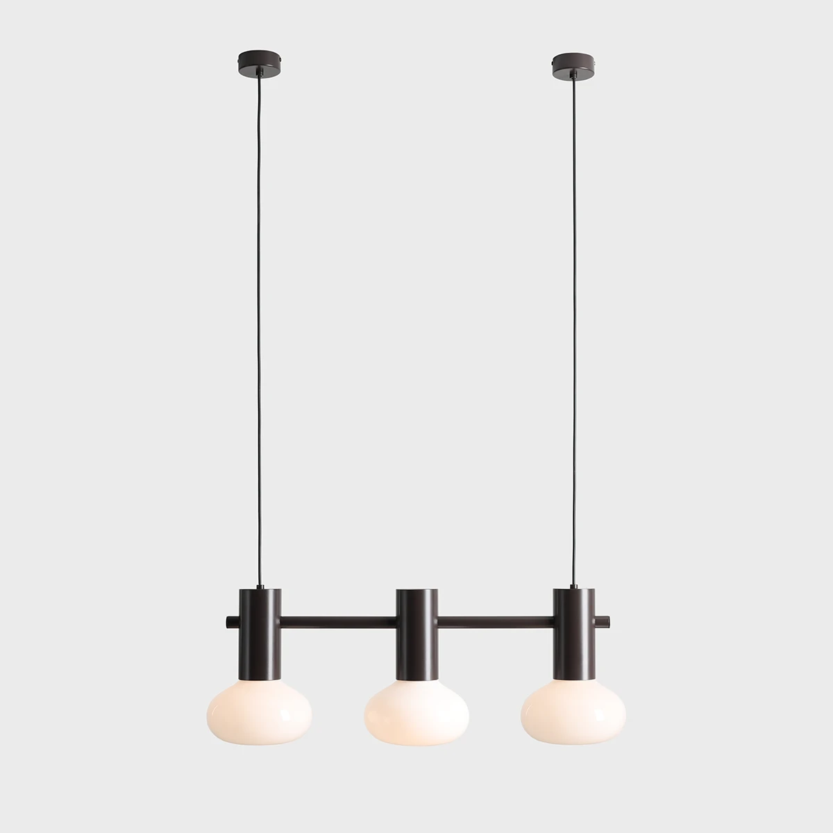 Lampa wisząca Flo Mokka z trzema źródłami światła E14. Metalowa konstrukcja w kolorze czarnym z trzema okrągłymi kloszami z mlecznego szkła. Zawieszona na dwóch przewodach, w surowym, minimalistycznym stylu. Tło jasnoszare.