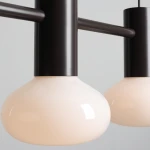 Lampa wisząca Flo Mokka z trzema oprawami E14, z metalowym, ciemnobrązowym stelażem oraz kulistymi kloszami w odcieniu kremowym. Ujęcie zbliżeniowe na klosze i elementy montażowe.