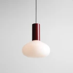 Lampa wisząca Flo Ruby D26 z kloszem w kształcie kulistym, wykonana z matowego szkła w kolorze białym. Posiada cylindryczny, ciemnoczerwony element montażowy. Zawieszona na cienkim czarnym przewodzie, prezentuje nowoczesny design.