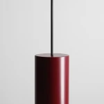 Lampa wisząca Flo Ruby D26 w kolorze czerwień burgundowa, o cylindrycznym kształcie, zawieszona na czarnym kablu. Produkt widoczny z boku, na jasnym tle, z gładką, błyszczącą powierzchnią. Wymagana żarówka E14.