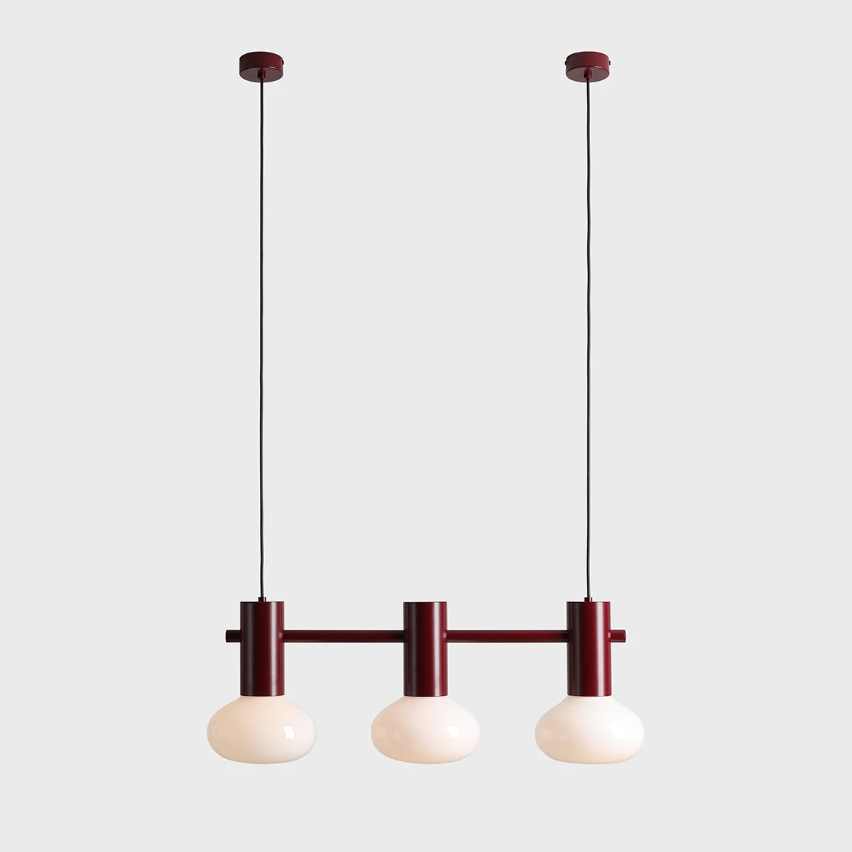 Lampa wisząca Flo Ruby z trzema źródłami światła E14. Metalowa konstrukcja w kolorze rubinowym z trzema okrągłymi, mlecznobiałymi kloszami. Produkt zawieszony na długim, czarnym przewodzie, umieszczony na jednolitym tle.
