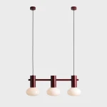 Lampa wisząca Flo Ruby z trzema źródłami światła E14. Metalowa konstrukcja w kolorze rubinowym z trzema okrągłymi, mlecznobiałymi kloszami. Produkt zawieszony na długim, czarnym przewodzie, umieszczony na jednolitym tle.