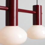 Lampa wisząca Flo Ruby w kolorze burgundowym z trzema kloszami w kształcie kul, wykonanymi z matowego szkła. Produkt zawieszony na czarnym przewodzie, z widocznym metalowym mocowaniem. Idealna do nowoczesnych wnętrz.