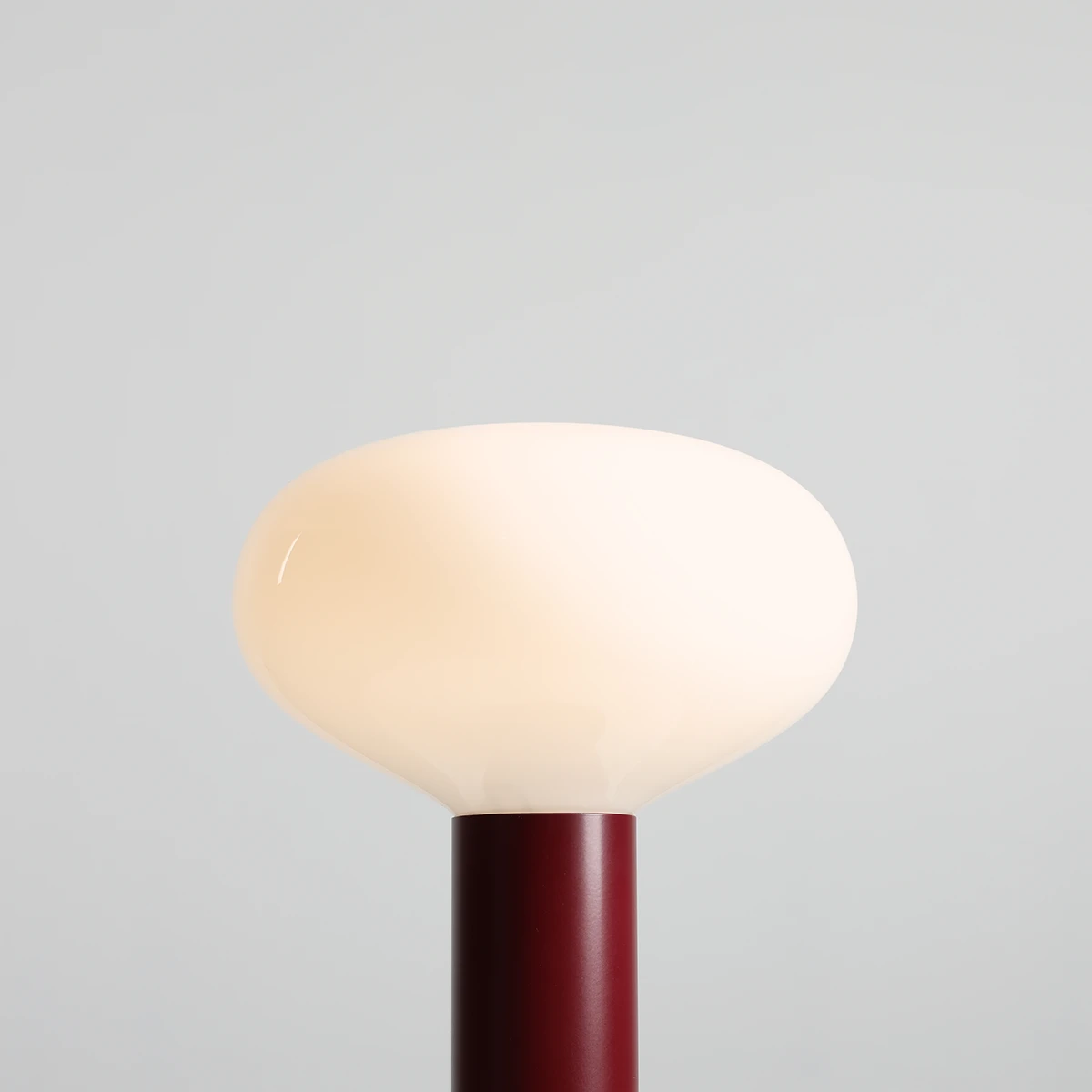 Duża lampa stołowa Flo Ruby z kloszem w kształcie półkuli w kolorze matowej bieli, umieszczona na cylindrycznej, burgundowej podstawie. Ujęcie z góry, pokazujące detale klosza i podstawy.