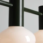 Lampa wisząca Flo Moss z trzema kloszami E14, z metalową, ciemnozieloną konstrukcją i matowym, jasnoróżowym szkłem. Ujęcie z bliska, pokazujące detal mocowania oraz kształt kloszy. Tło jasnoszare, minimalistyczne.