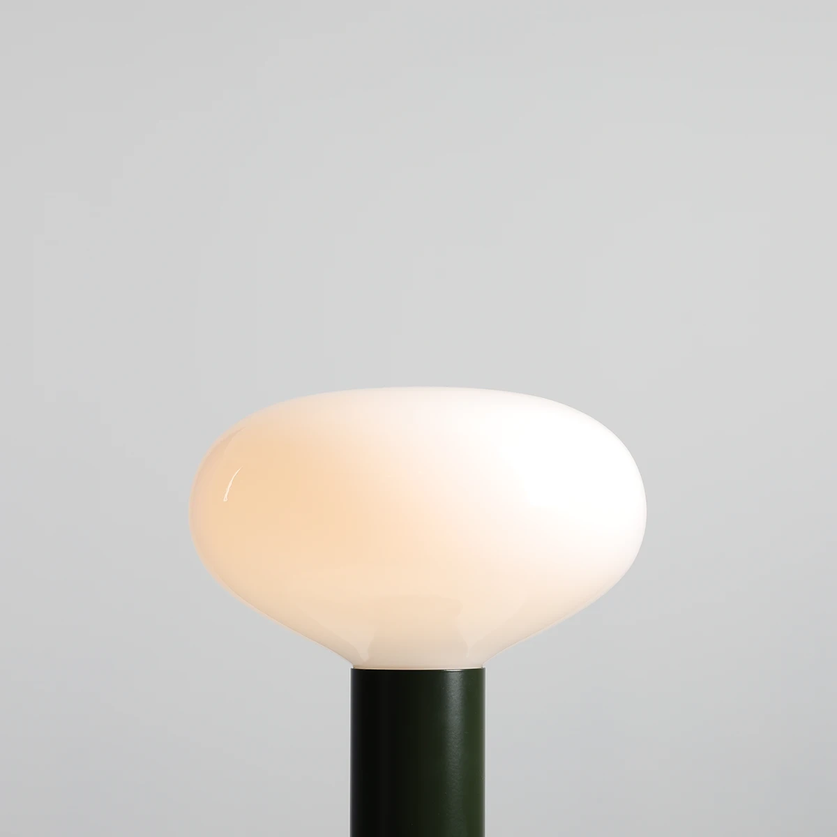 Lampa stołowa Flo Moss z dużą, okrągłą, matową kloszem w kolorze białym, osadzona na zielonym, metalowym trzonie. Ujęcie z góry, pokazujące kształt klosza i jego fakturę na jednolitym tle.