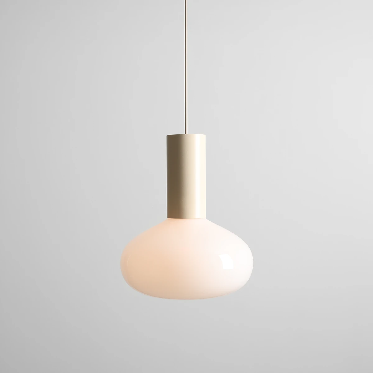 Lampa wisząca Flo Cream D26 z kloszem w kształcie kuli w odcieniu mlecznym, z metalowym, złotym uchwytem. Zawieszona na cienkim przewodzie, w prostym otoczeniu na szarym tle. Przeznaczona na żarówkę E14.