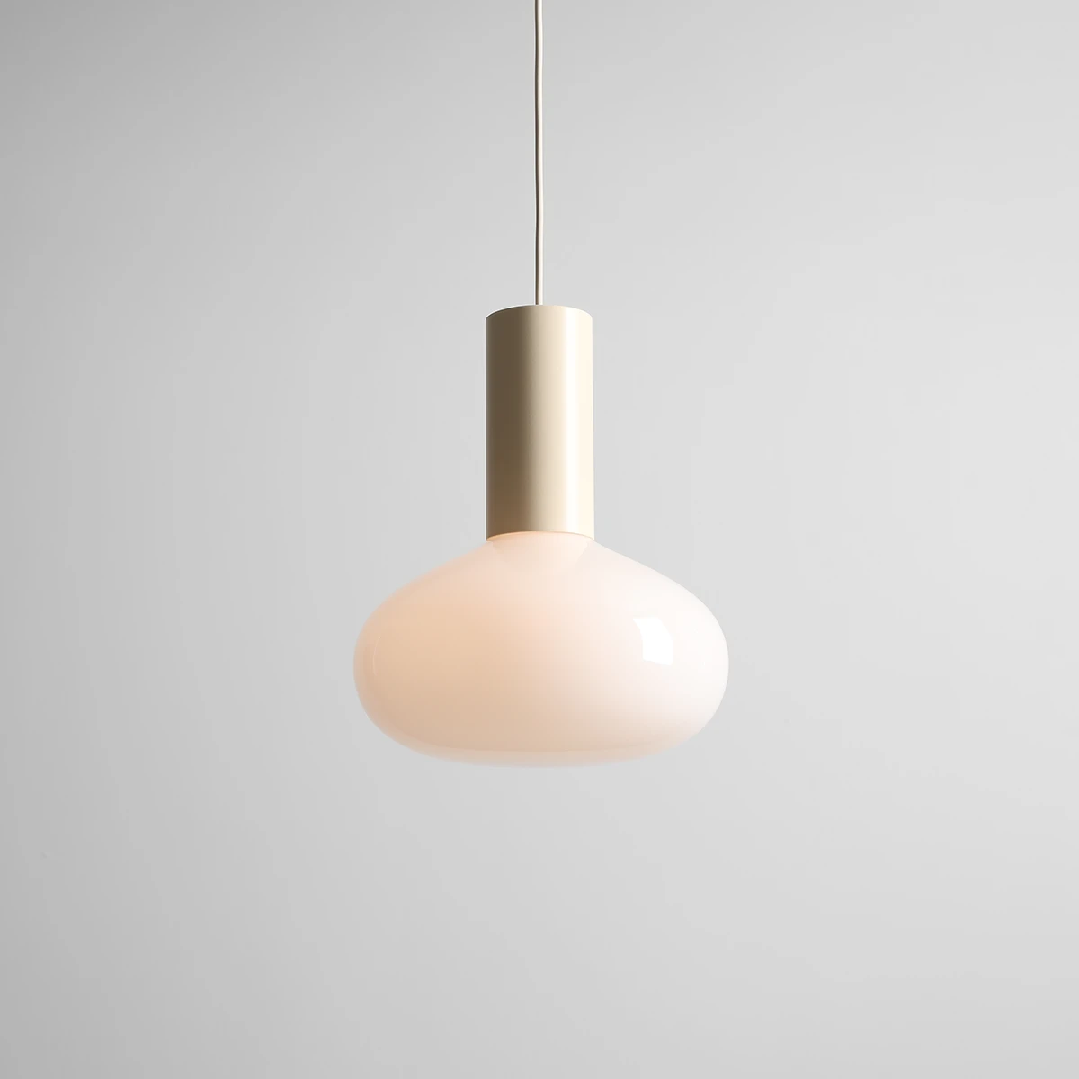 Lampa wisząca Flo Cream D26 z kloszem w delikatnym odcieniu kremowym, z metalowym, złotym trzonkiem. Ujęcie frontalne, zawieszona na cienkim przewodzie. Idealna do nowoczesnych wnętrz. Wymiary i szczegóły montażu nie są widoczne.