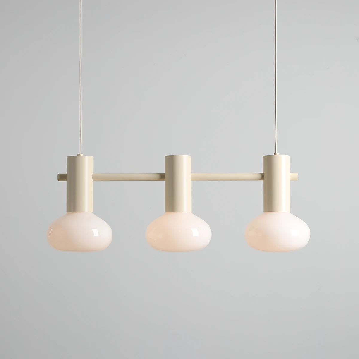 Lampa wisząca Flo Cream z trzema kloszami E14 w kształcie kulistym, wykonana z mlecznego szkła. Utrzymana w jasnej, kremowej kolorystyce, zawieszona na prostym metalowym stelażu. Produkt prezentowany na jednolitym tle.