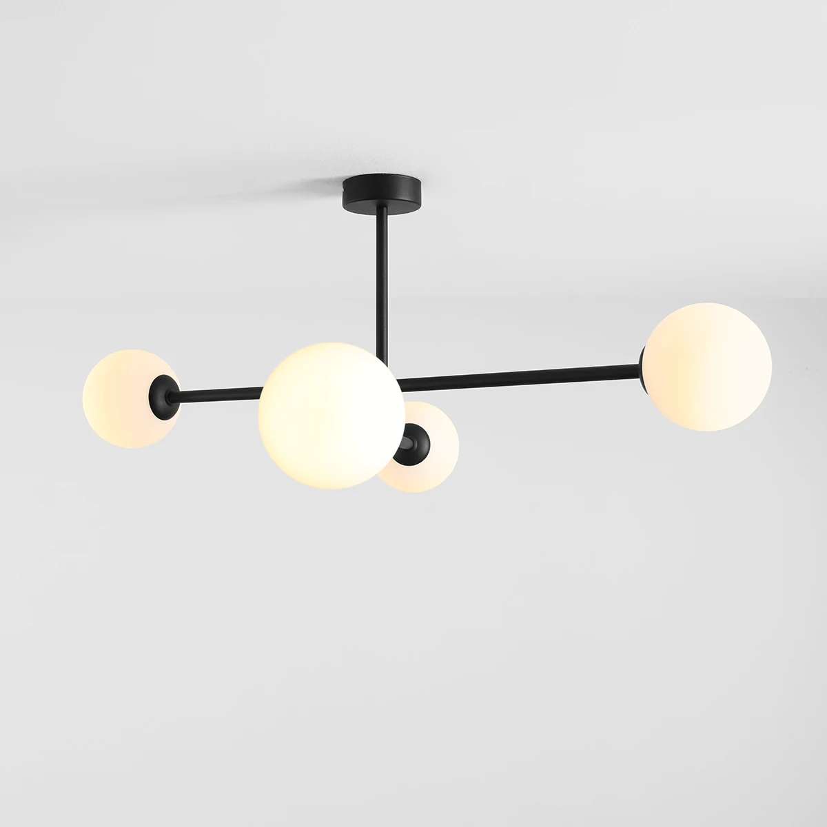 Czarna lampa sufitowa Pinne z czterema oprawami E14, z kulistymi kloszami w kolorze białym. Produkt zamontowany na suficie, z widocznymi metalowymi ramionami w minimalistycznym stylu.