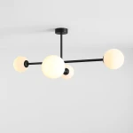 Czarna lampa sufitowa Pinne z czterema oprawami E14, z kulistymi kloszami w kolorze białym. Produkt zamontowany na suficie, z widocznymi metalowymi ramionami w minimalistycznym stylu.