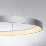 Lampa wisząca LED Hoop w kształcie koła, o mocy 37W i barwie światła 3000K. Posiada aluminiowy, matowy klosz z białym, emitującym światło obrzeżem. Zawieszona na cienkich linkach, widoczna z boku, na jednolitym tle.