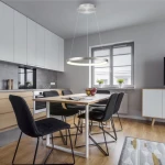 Lampa wisząca LED Hoop koło 37W 3000K w kolorze aluminium, zawieszona nad drewnianym stołem w nowoczesnej kuchni. W tle widoczne czarne krzesła i okno z roślinami. Oświetlenie daje ciepłe światło, podkreślając minimalistyczny design wnętrza.