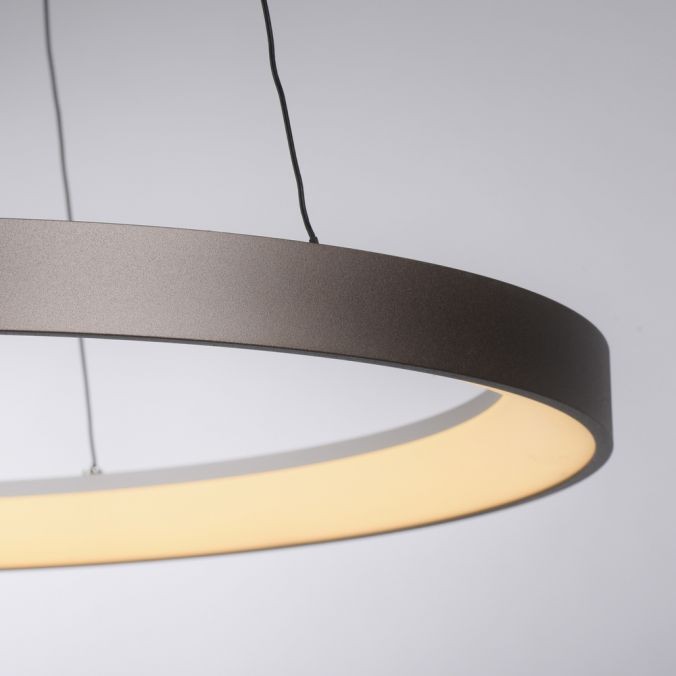 Lampa wisząca LED Hoop w kształcie koła o mocy 37W i temperaturze barwowej 3000K. Posiada matową, kawową obudowę i emitujący ciepłe światło, zawieszona na cienkich przewodach, widoczna z boku.