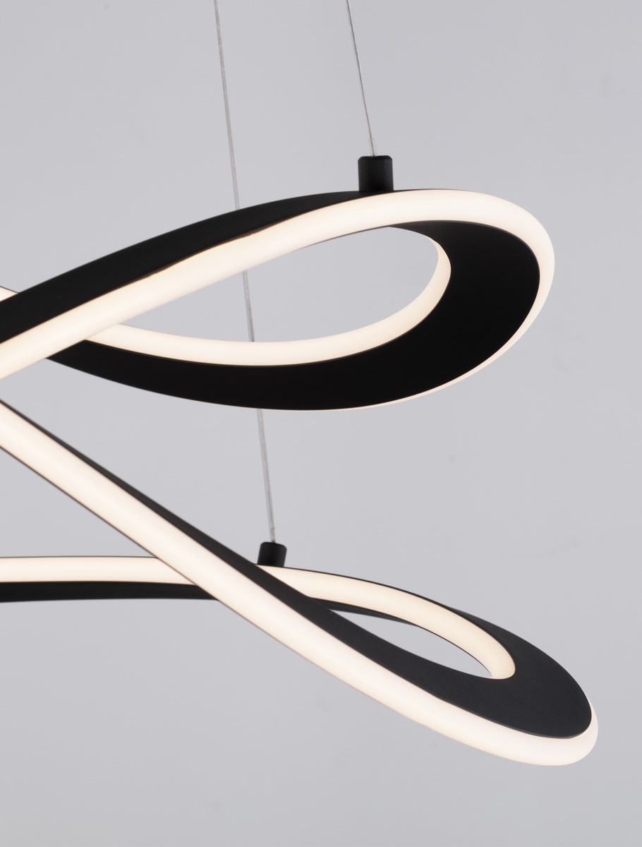 Lampa wisząca Jauja z dwoma źródłami światła LED, 87W, w kolorze czarnym. Wykonana z materiału w formie falistej, z białym oświetleniem LED wzdłuż krawędzi. Zawieszona na cienkich linkach, z widocznym mocowaniem. Tło w jasnym kolorze.