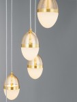 Lampa wisząca Arena z pięcioma kulistymi kloszami, w kolorze czarnym i złotym, z białym, matowym szkłem. Klosze wiszą na białych przewodach, w minimalistycznym układzie. Tło szare, podkreślające elegancję lampy.