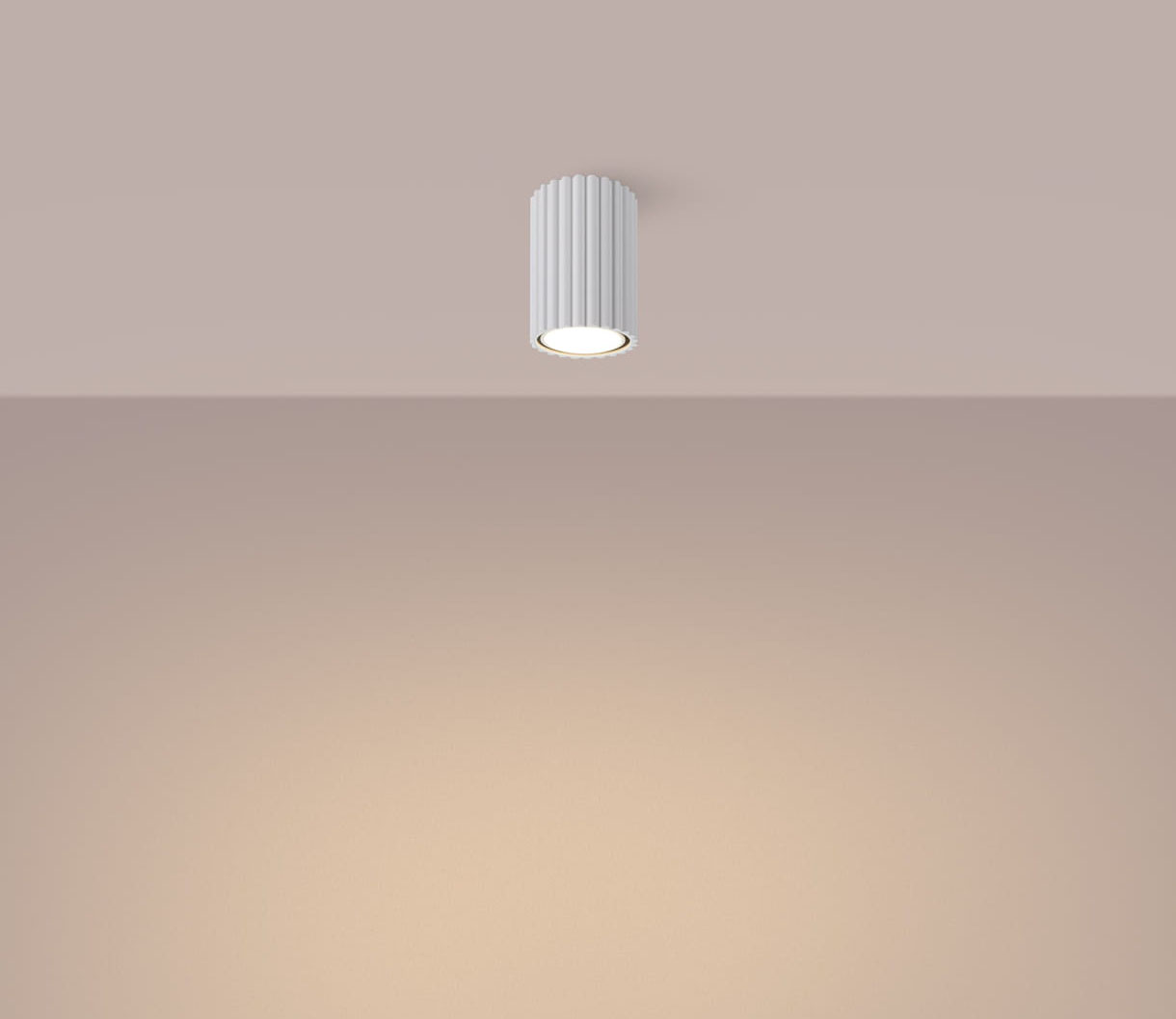 Biała lampa sufitowa Karbon 10 z jednym gniazdem GU10, o cylindrycznym kształcie z pionowymi żłobieniami. Zawieszona na suficie, oświetla przestrzeń delikatnym światłem, na jednolitym, jasnym tle.