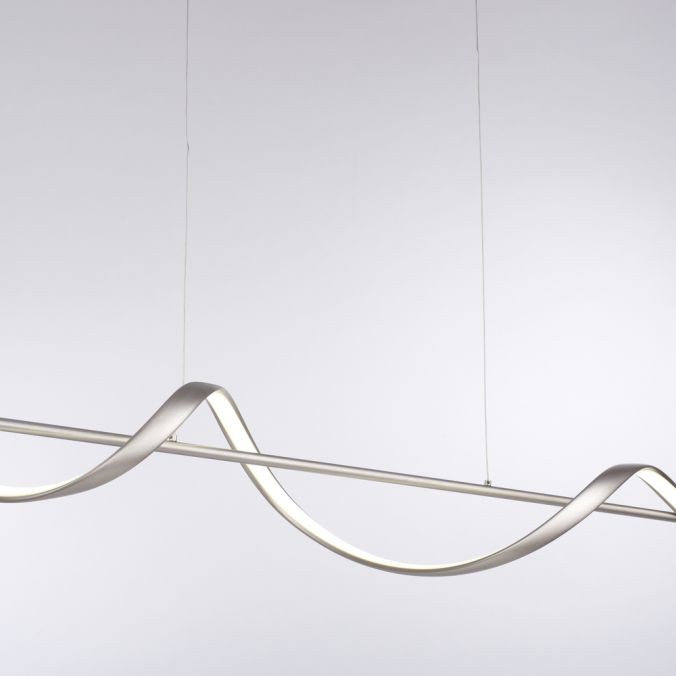 Lampa wisząca Q-swing w kolorze niklu satynowego, z elastycznym kształtem fali. Posiada zintegrowane oświetlenie LED 28W CCT, zawieszona na cienkich linkach. Pilot umożliwia zdalne sterowanie. Tło proste, jasne.