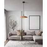 Czarna lampa wisząca Peca z brązowym kloszem LED 12W, zawieszona na cienkim kablu, w nowoczesnym wnętrzu z jasną sofą i okrągłym stołem. Tło z minimalistycznym obrazem i rośliną w doniczce.