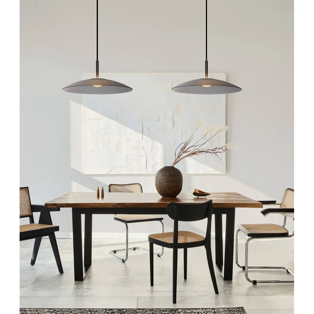 Lampa wisząca Peca z szarym kloszem i czarnym zawieszeniem, montowana nad drewnianym stołem. W tle widoczne krzesła z wiklinowymi siedziskami i dekoracyjny wazon. Minimalistyczne wnętrze z jasnym tłem i subtelnym oświetleniem.
