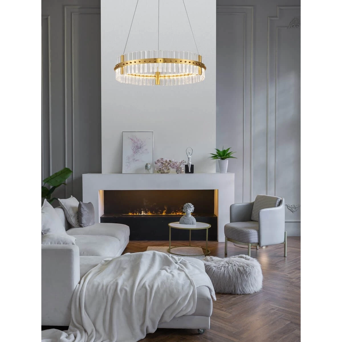 Lampa wisząca Mayo D60 z jedną żarówką LED 45W, złota, okrągła konstrukcja z przezroczystymi elementami, zawieszona nad kanapą w nowoczesnym wnętrzu z kominkiem. Tło jasne, drewniana podłoga, stylowe meble obok.
